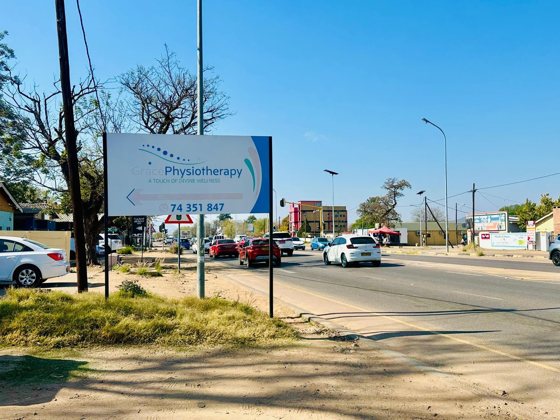 The Grace Physiotherapy roadside signboard on Kaunda Road pointing towards the clinic and showing the branch phone number.