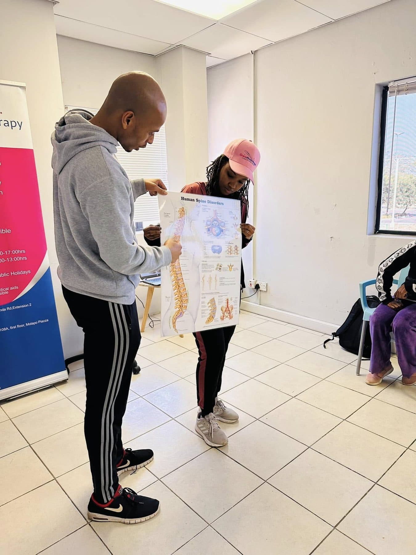 A Grace Physiotherapy therapist explaining spinal anatomy from a wall chart with a patient.